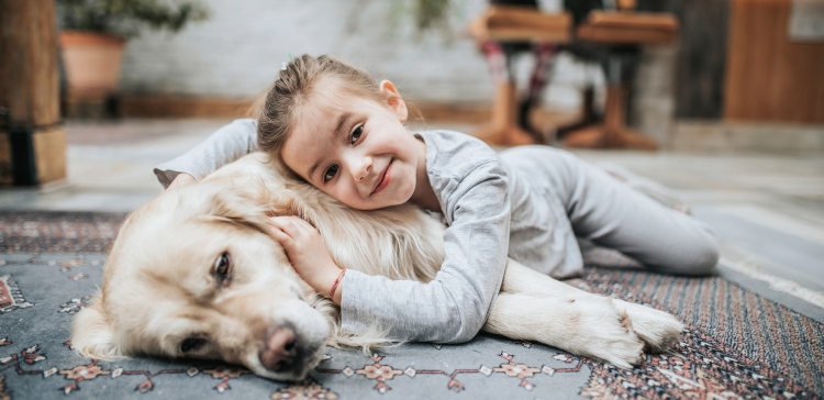 Cute little girl relaxing with her dog on carpet at home and looking at camera.