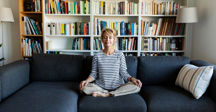 Mature woman practicing yoga on couch at home