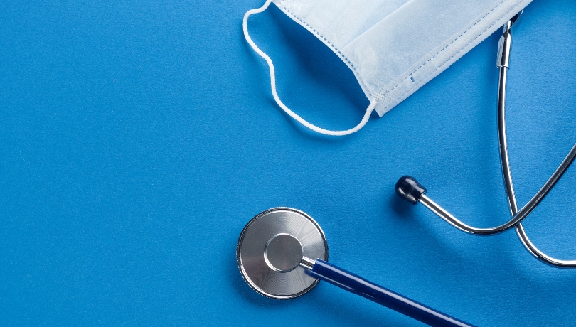 Protective Disposable Medical Face Mask And Stethoscope On A Blue Background.
