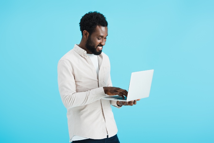 smiling african american man in white shirt using laptop isolated on blue