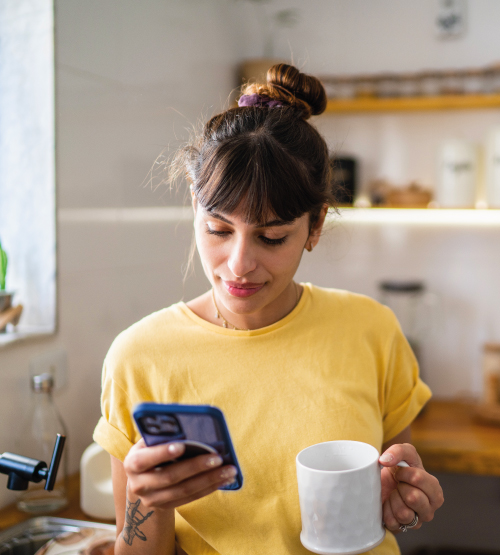 Mujer sostiene y observa su celular mientras está tomando un café