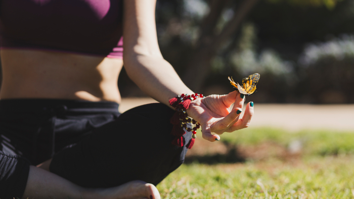 joven sentada en el pasto con mariposa en la mano