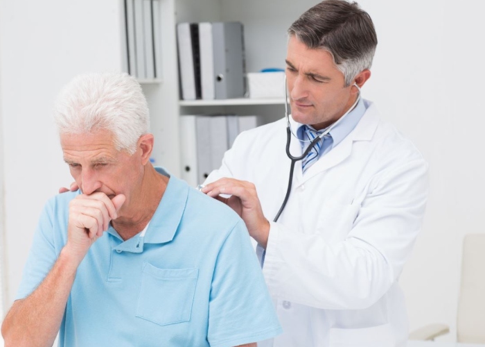 Hombre mayor tosiendo mientrás un médico lo examina 