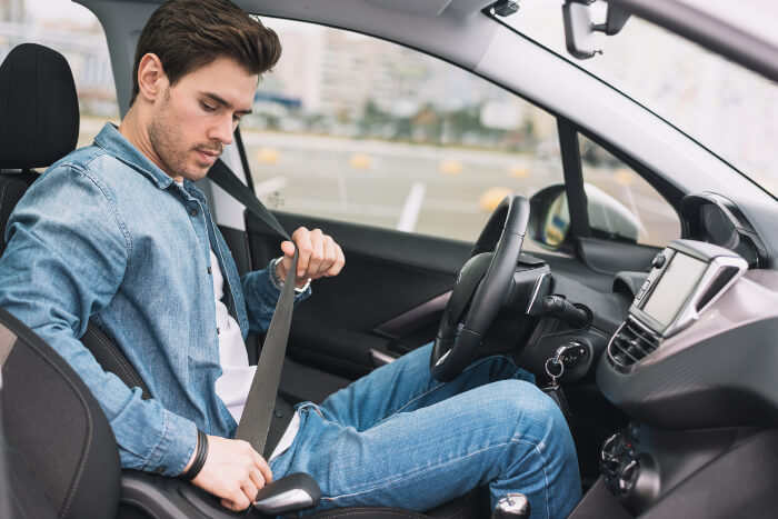 Hombre sentado en un auto, colocándose el cinturón de seguridad 