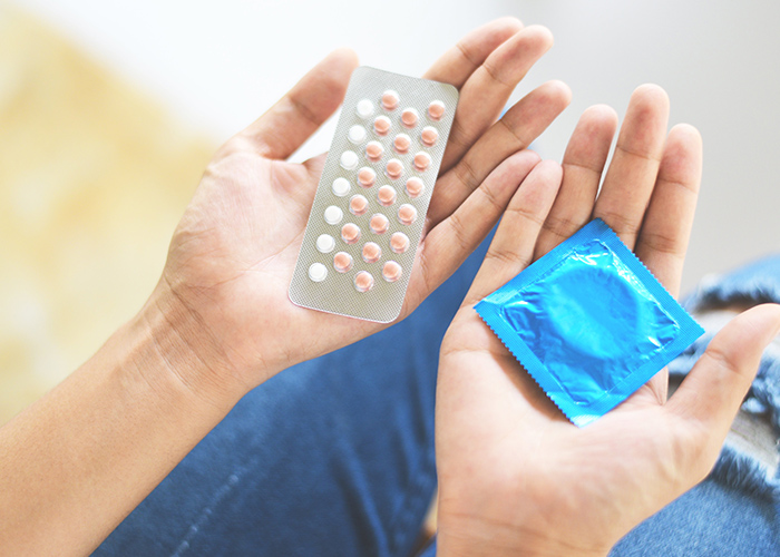 Pastillas anticonceptivas y condón sobre cada mano