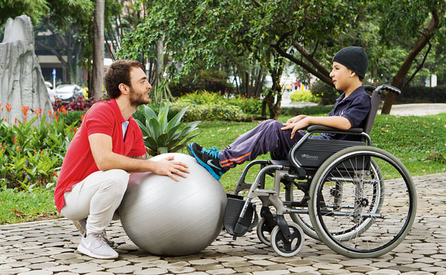 Cuidador haciendo ejercicios con niño en silla de ruedas