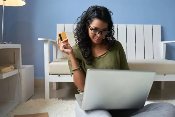Mujer sentada frente al computador con una tarjeta bancaria en la mano
